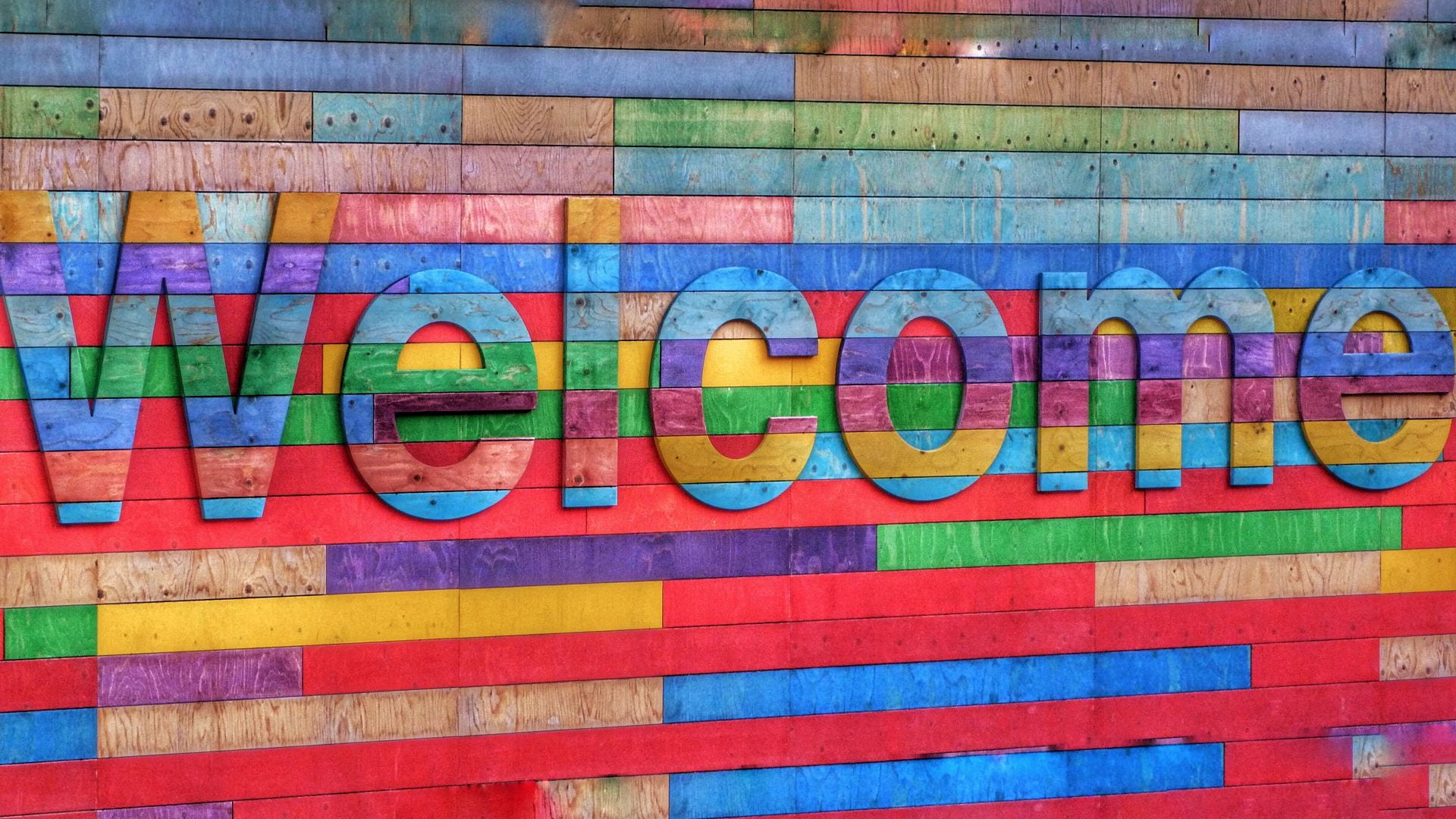 Multicoloured wooden wall with a 3D releif saying Welcome