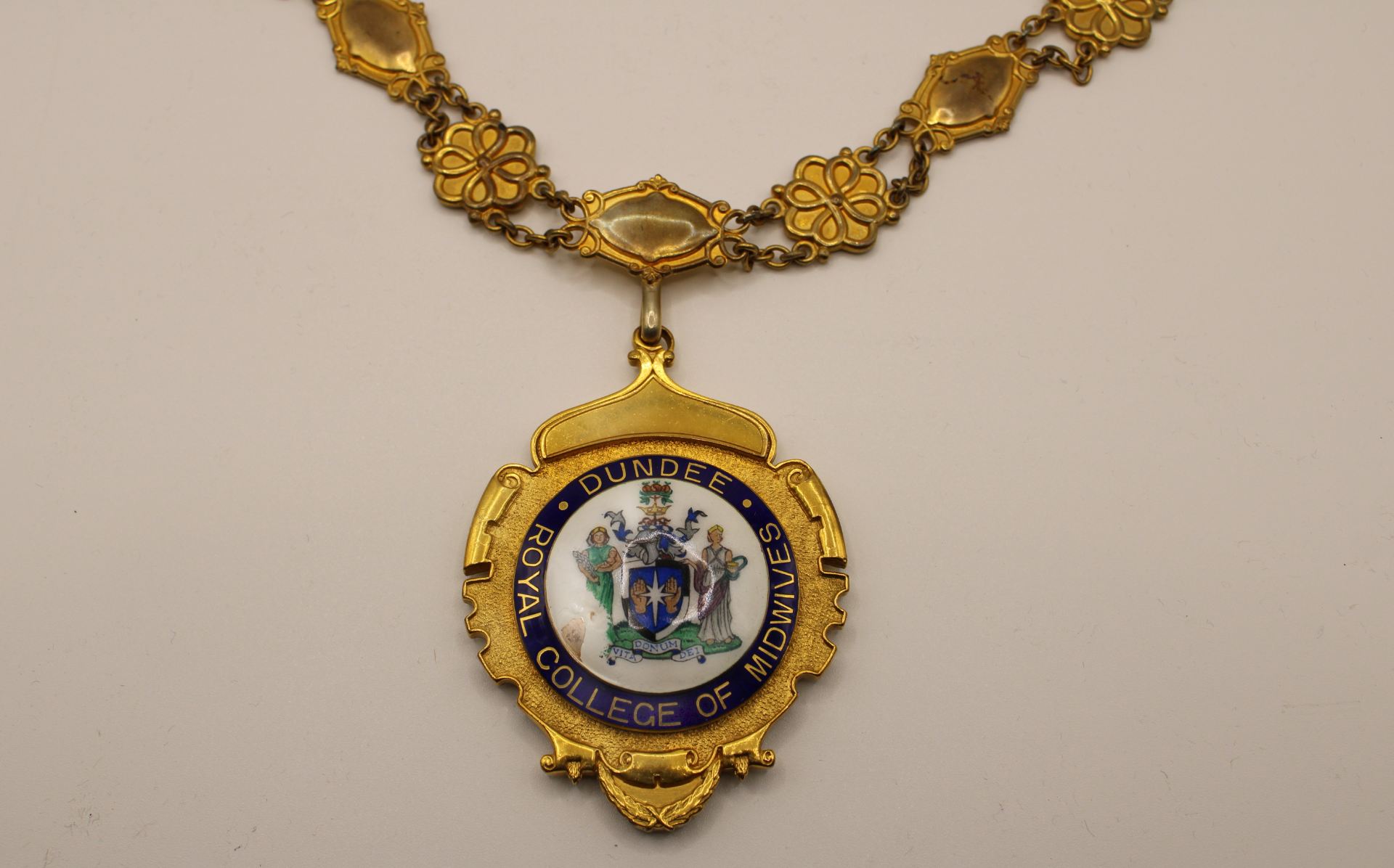 A gold chain with the emblem of the Dundee branch of the Royal College of Midwives hanging from the centre. 